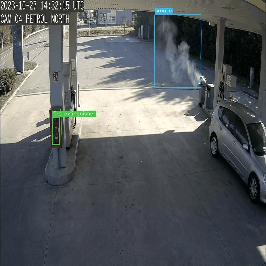 营业中的加油岛，远处设施侧冒烟。泵柱上的灭火器被索引，告警可指向最近器材。